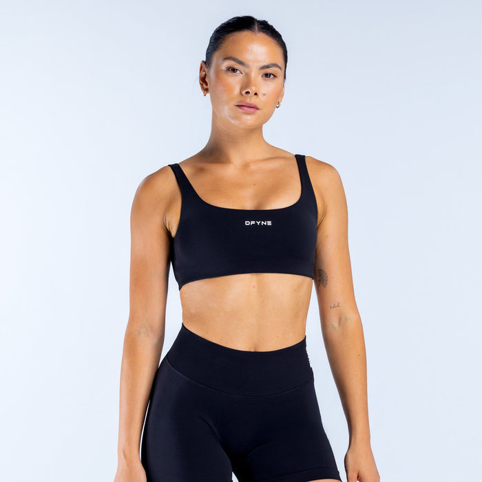 Black scoop-back sports bra with wide straps and DPYNE logo on front.