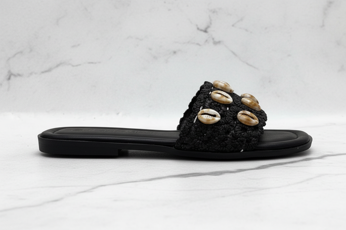 Evani Black Cowrie Shell Raffia Flat Slide Sandals – side profile view on white marble