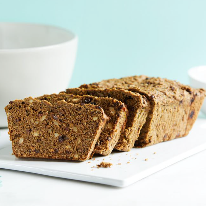 Loaf of banana bread with slices on a white plate against a light blue background