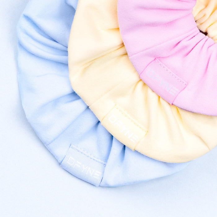 Scrunchie close-up in pink and cream fabric, stitched logo detail on gathered band