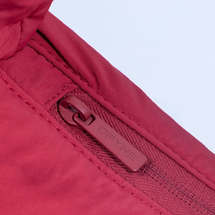 Red puffer bag zipper with branded pull tab and stitched edge.