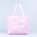 Light pink tote bag with wide handles and vertical logo tape on each side.