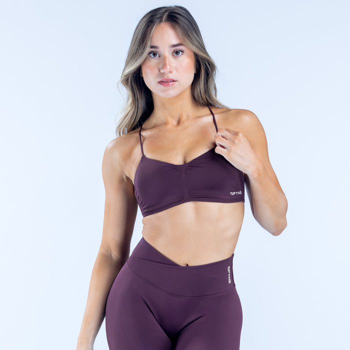 Plum sports bra with thin spaghetti straps and small printed logo at hem